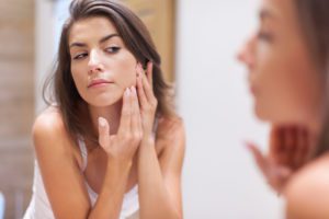 woman looking in the mirror debating on botox and if it will help her acne