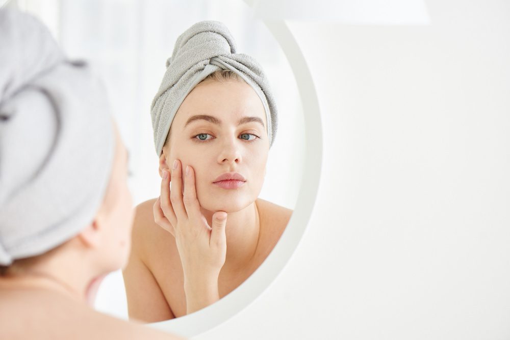 young woman looking in the mirror at her face considering getting botox in Los Angeles.