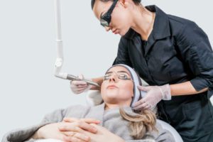 Beauty laser technician performing a cosmetic skin resurfacing session on a female patient, also called a photofacial