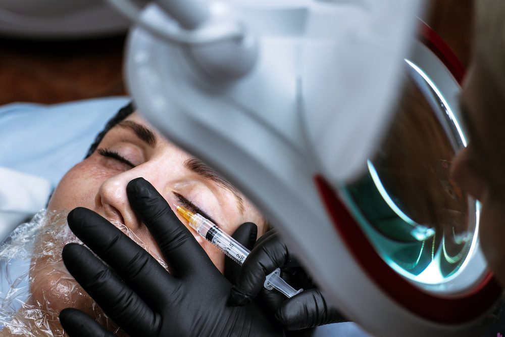 Beautician makes an injection of beauty. The doctor injects an injection under the eyes of a young woman. Cosmetologist services.
