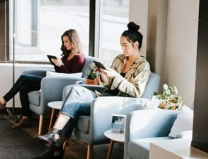 Two women using their gadgets while sitting on chairs
